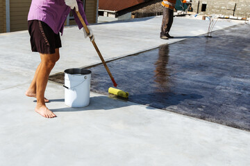 A worker varnishes the floor surface on an outdoor veranda. Finishing of the adjacent territory....