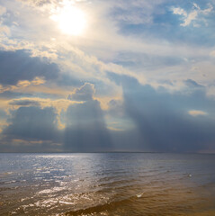 Naklejka na ściany i meble sun push through the dense clouds over a sea bay