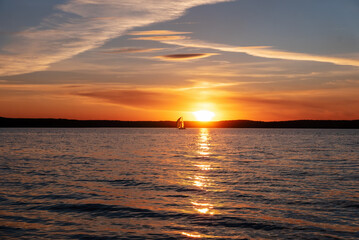 Fototapeta premium Peaceful sunset on the sea. Sailing yacht on the background of the setting sun. Focus on the foreground