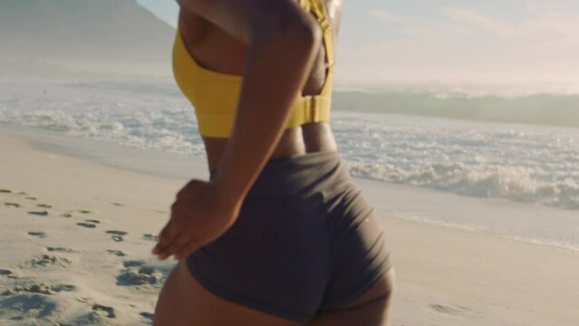 A fit, dedicated and healthy woman wearing fitness clothes running on sand on a peaceful beach. A sweating and athletic female jogging in slow motion on nice sunny day listening to workout music