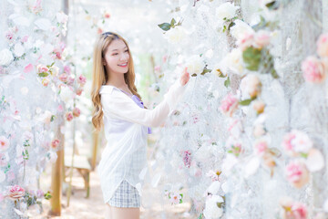 Asian beautiful woman blonde wearing a purple shirt while smiles and stands in white rose flower garden as natural , luxury theme