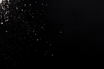 Flying white flour, powder on a black background. Spray of particles, lumps, pieces of white...