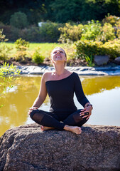 Naklejka na ściany i meble young beautiful woman doing yoga exercises on the stone near lake in the park