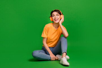 Full body photo of minded cheerful girl arm touch headphones look interested empty space isolated on green color background