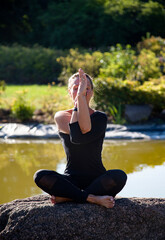 Fototapeta na wymiar young beautiful woman doing yoga exercises on the stone near lake in the park