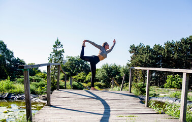 Fototapeta premium woman practicing yoga in the park on old bridge in summer sunny morning