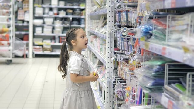 A little girl in a supermarket is looking at a shelf with stationery. Preparation for school and kindergarten. The child chooses a toy for himself.Racks with goods