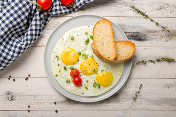 Fried eggs with tomatoes, toasts and green onion on white wooden table top view
