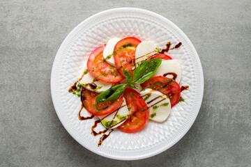 Caprese salad with mozzarella and tomato with basil and balsamic and pesto sauce on white plate top view on grey table