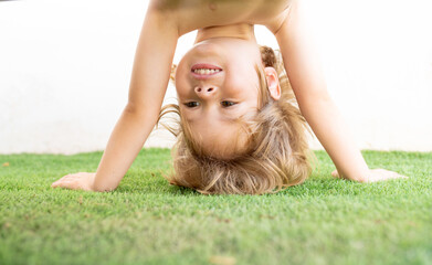 Cute smiling little boy doing a handstand on the grass.