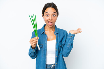 Young hispanic woman holding chive isolated on white background with shocked facial expression