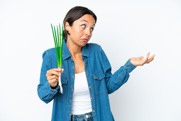 Young hispanic woman holding chive isolated on white background with surprise expression while looking side
