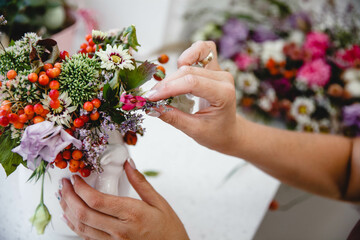 A woman florist makes a small bouquet of fresh flowers in a white vase with decorative rabbits at a...