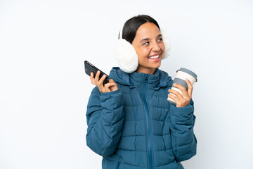 Young hispanic woman wearing a winter earmuffs isolated on white background holding coffee to take...