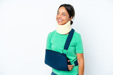 Young hispanic woman wearing a neck brace and sling isolated on white background looking side