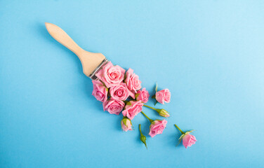Paintbrush with pink roses on the blue background. Top view. Copy space.