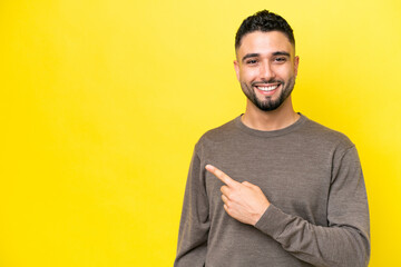 Young Arab handsome man isolated on yellow background pointing to the side to present a product