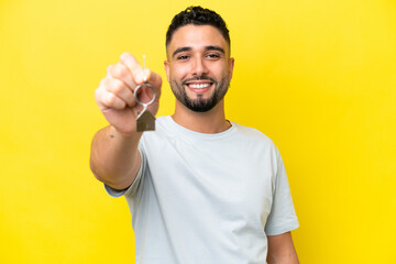 Young Arab man holding home keys isolated on yellow background with happy expression