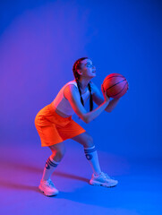 Fototapeta premium girl with a basketball in orange shorts, a t-shirt. an athlete in golfs and sneakers on a blue background plays the ball. Physical education teacher. basketball player. in move. blur. the game