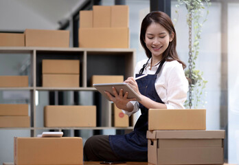 Fototapeta na wymiar Young beautiful happy asian business woman owner of SME online using laptop receive order from customer with parcel box packaging at her startup home office, online business seller and delivery