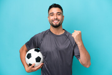 Young Arab handsome man isolated on blue background with soccer ball celebrating a victory