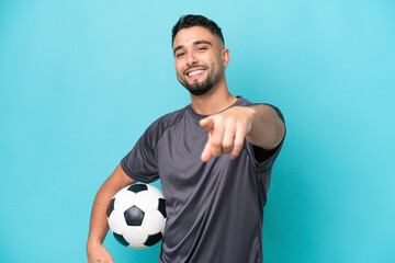 Young Arab handsome man isolated on blue background with soccer ball and pointing to the front
