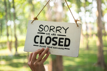 "Sorry, Closed" wooden sign tag of cafe or restaurant is turning by human's hand, with background of outdoor environment. Sign and symbol object photo.