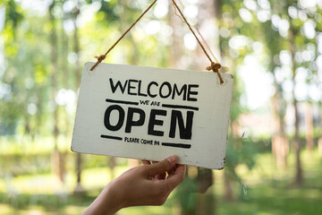 Action of human's hand flipping the "Welcome, Open" banner sign of the cafe, with background of outdoor environment. Sign and symbol for business object photo.