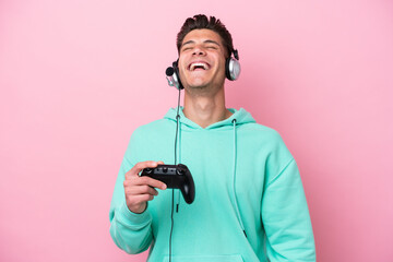 Young handsome caucasian man playing with a video game controller isolated on pink background laughing