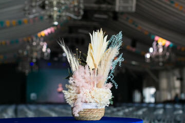 A composition of dried and colored leaves and flowers of plants in a cylindrical wicker basket as an event or home decoration.