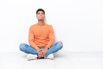 Young man sitting on the floor isolated on white background and looking up