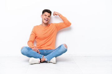 Young man sitting on the floor isolated on white background doing strong gesture