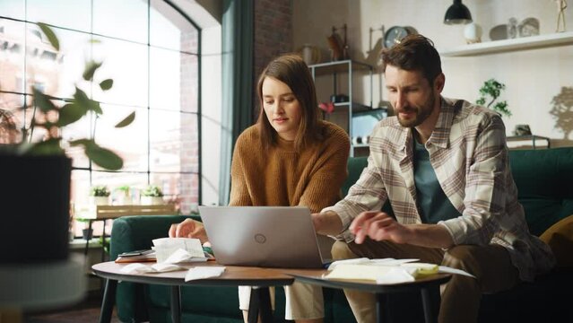 Doing Accounting at Home: Happy Couple Using Laptop Computer, Sitting on Sofa in Apartment. Young Family Filling Tax Forms, Mortgage Documents, Bills, Checks, Balances, Invoices are in Order