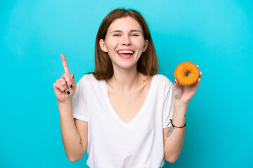 Young English woman holding a donut over isolated blue background pointing up a great idea