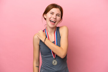 Young English woman with medals isolated on pink background celebrating a victory