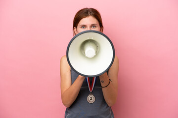Young English woman with medals isolated on pink background shouting through a megaphone