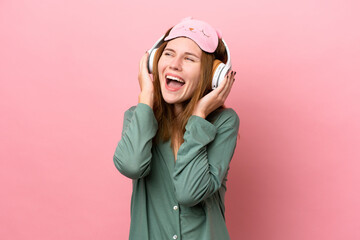 Young English woman in pajamas isolated on pink background in pajamas and holding a pillow and listening music