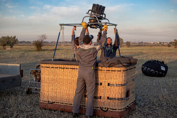 several people in uniform at dawn in the summer install a burner on the basket of a hot air balloon...