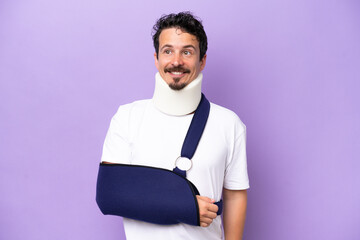 Young caucasian man wearing a sling and neck brace isolated on purple background thinking an idea while looking up