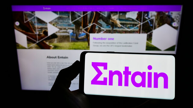 Stuttgart, Germany - 01-08-2022: Person holding smartphone with logo of sports betting company Entain plc on screen in front of website. Focus on phone display.
