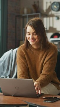 Smiling Young Woman Working from Home on Laptop Computer in Her Sunny Cozy Apartment, Relaxes and Leans Back on a Sofa. Successful Creative Female Entrepreneur Happy After Finishing Remote Work