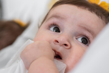 close-up of the face of a beautiful baby with a curious look at her mother, sticking a finger in...