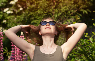 young girl in sunglasses with red hair in the nature among lupins