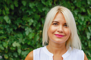 Naklejka premium Portrait of a middle-aged woman against a background of green leaves. Success, antiaging