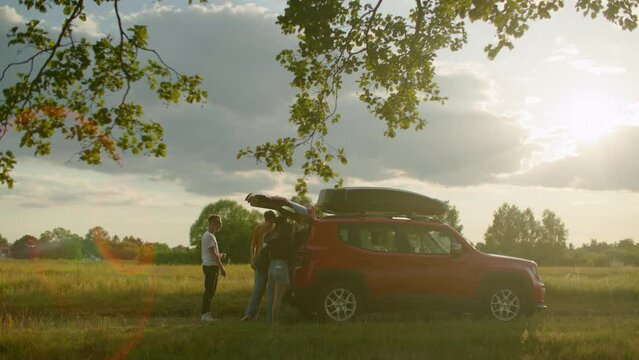 Traveling Friends take out things, close car trunk and go to Camping or Picnic. Group of four multi-cultural young people spend active weekend together in summer. 4k cinematic wide gimbal shot