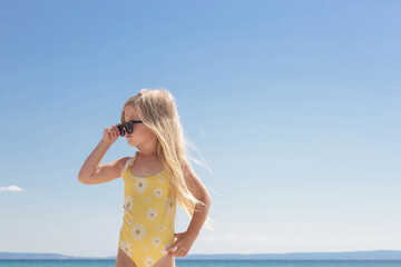 Portrait of 4 years old girl in yellow swimsuit and long blonde hair with blue sea and sky on the...