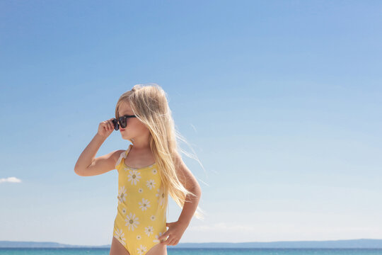 Portrait of 4 years old girl in yellow swimsuit and long blonde hair with blue sea and sky on the sandy beach