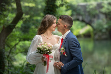 a guy in a suit and a girl in a white dress are standing in the forest and hugging.