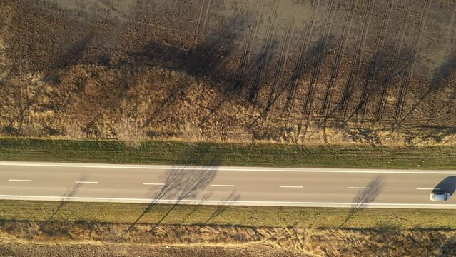 Top down aerial footage of car breaking speed limit on highway through countryside landscape in autumn afternoon