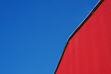 Abstract architecture. Detail of red building facade with metal siding on blue sky, nobody. Low angle view